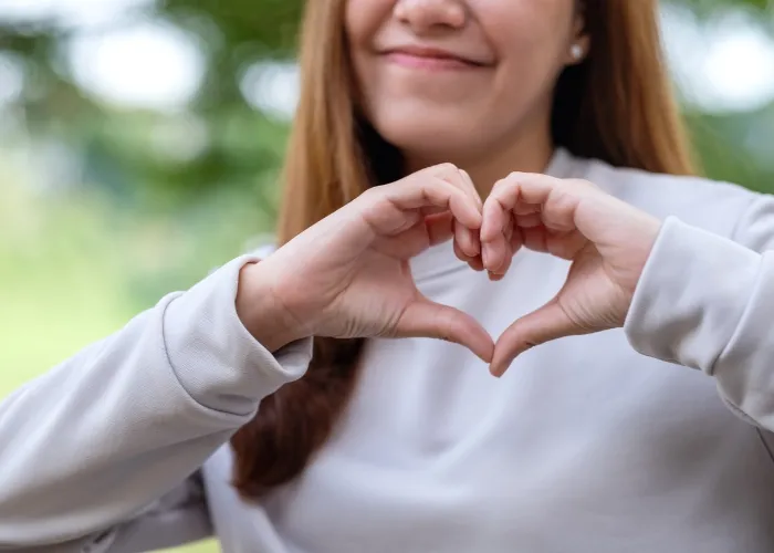 Closeup image of a young woman making heart hand sign