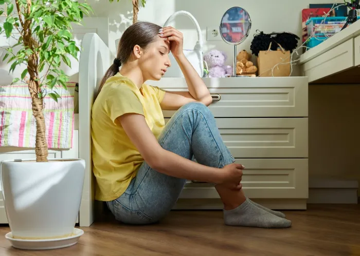 Sad teenage girl sitting on the floor at home. Upset female high school student in room. Teenage problems, stress, depression, adolescence, mental health concept